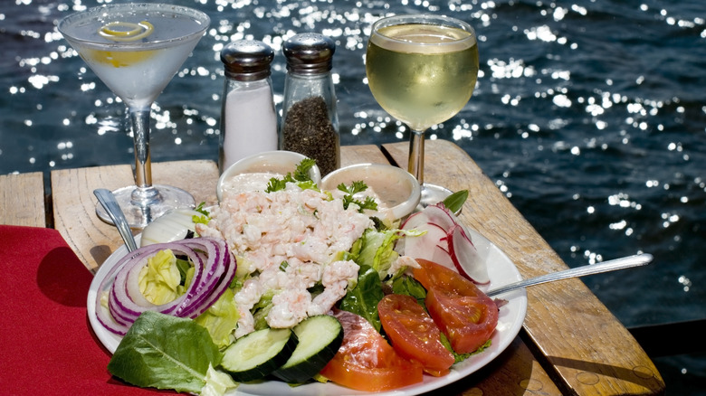 A crab louie salad on a wooden table with a martini glass and white wine