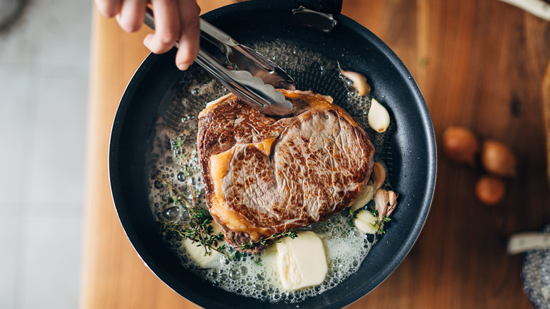 Steak sizzling in a pan with butter in it. 