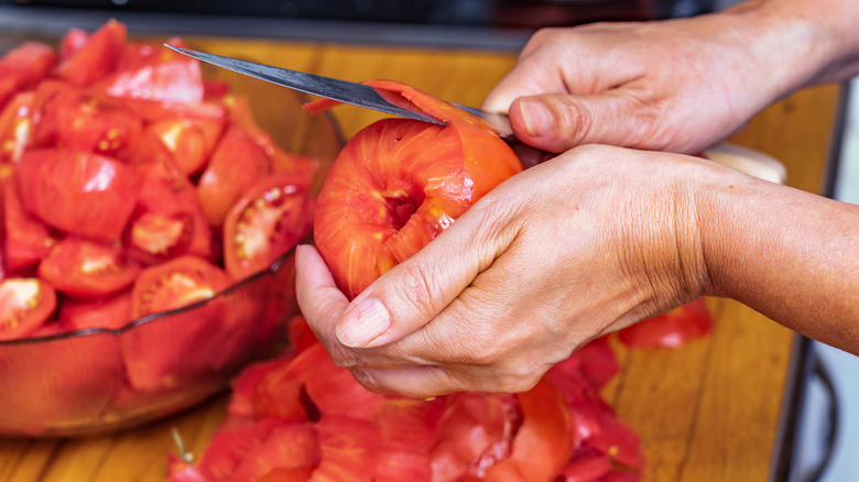 hands removing the skin from a red tomato