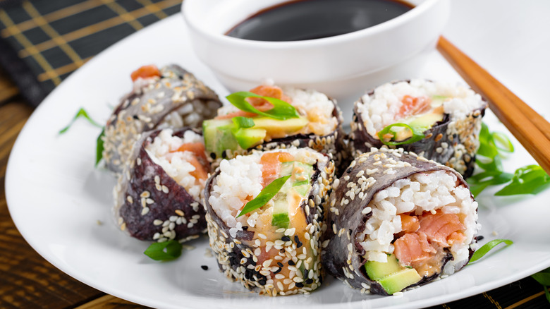 A sushi roll on a white plate with soy sauce