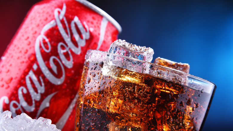 A sweaty, ice-filled glass of Coca-Cola in front of a can of Coca Cola