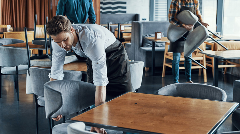 A server stacking chairs on a restaurant patio.