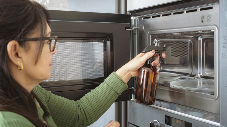 Woman spraying microwave oven interior with vinegar