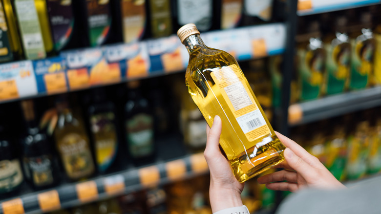 A person's hands are seen holding a glass bottle of cooking oil in a market.