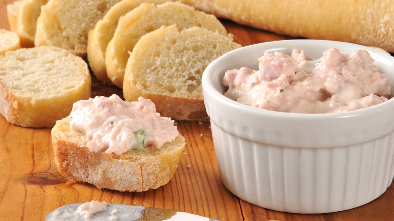 A spread or dip of deviled ham in a ramekin, some spread over a slice of baguette with more sliced baguette in the background.