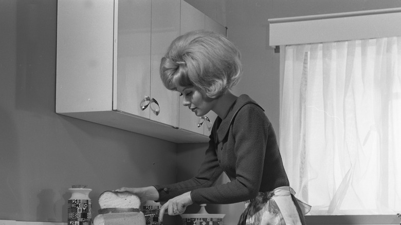 Vintage black-and-white image of a person in a kitchen preparing a meal
