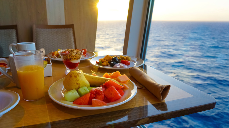 Table with cruise breakfast buffet items on it next to a window view of the ocean