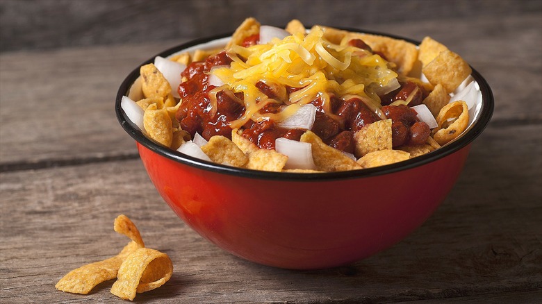 Corn chips, saucy beans, chopped onion, and shredded cheese in a small red bowl with a black rim