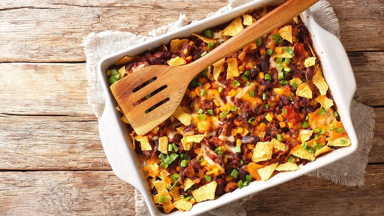 Frito pie in a rectangular baking dish with a slotted wooden spoon