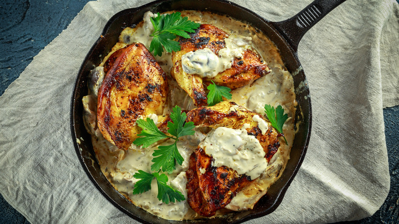Roasted chicken supreme with creamy mushroom sauce and herbs in a cast iron skillet on beige cloth.