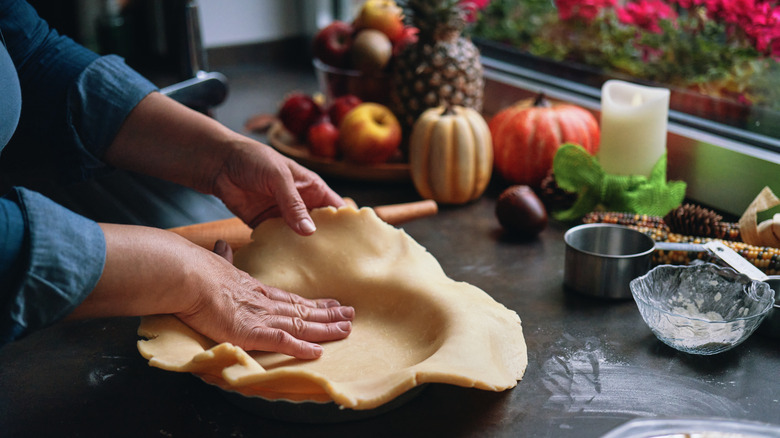 A person's hands are seen pressing crust into a pie tin.
