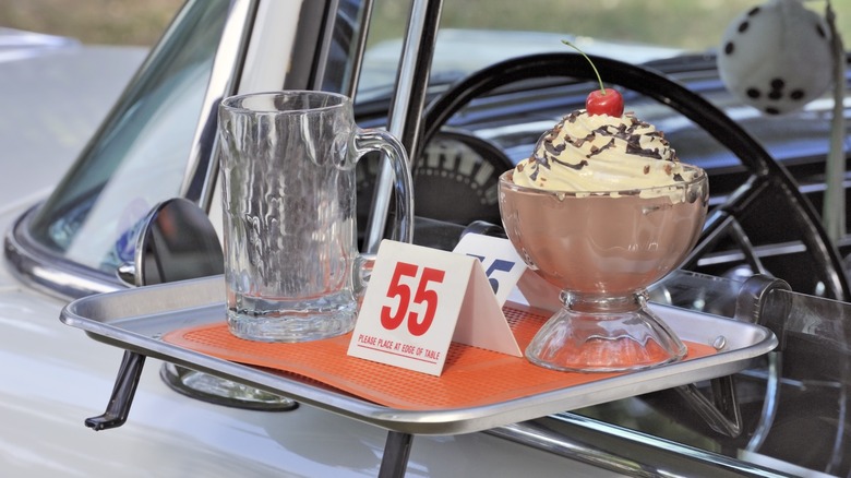 a chocolate ice cream sundae and glass mug at a retro drive-in display