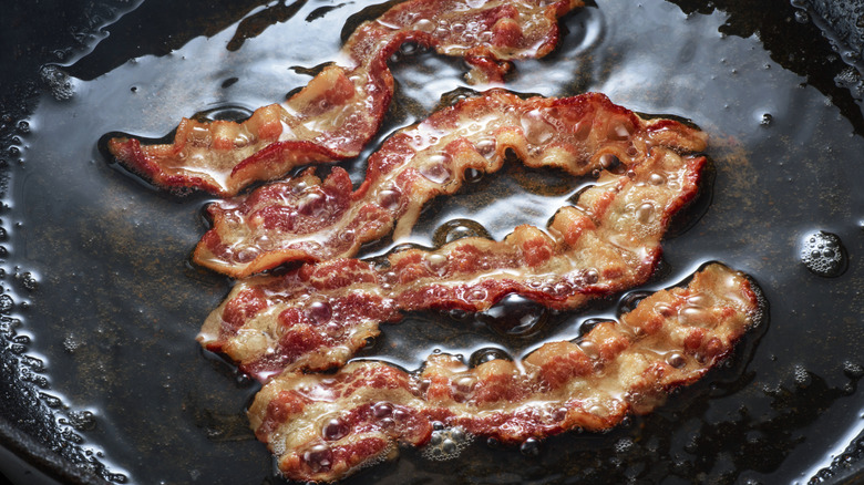 Four strips of bacon sizzling in grease in a pan.