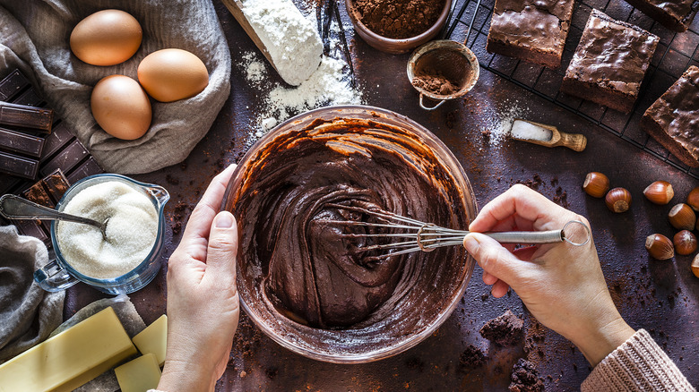 Hands mixing a chocolatey batter with a whisk.