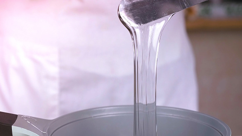 Liquid glycerin dripping into a bowl or measuring spoon.