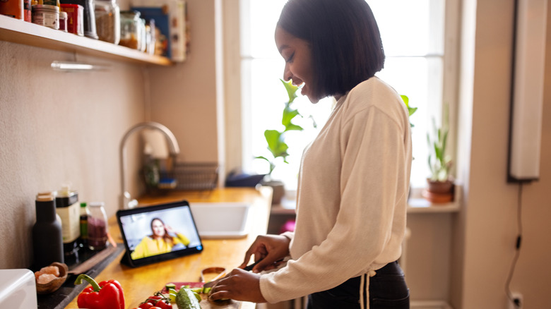 A person chops vegetables on a kitchen counter beside a tablet