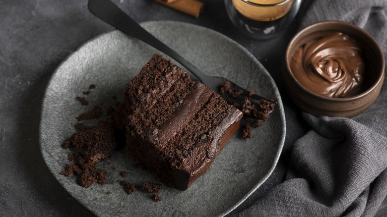 A slice of chocolate cake on a plate, next to a bowl of chocolate
