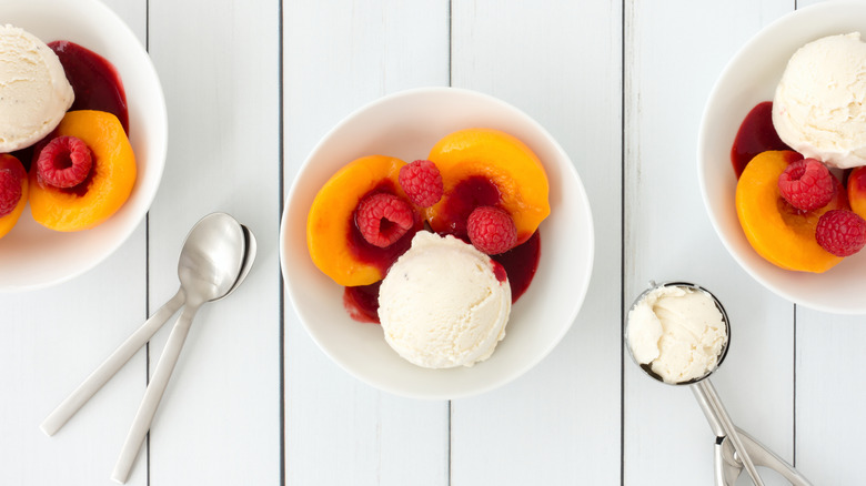 A bowl of peach melba containing peaches, raspberry sauce, and vanilla ice cream, is photographed from above.