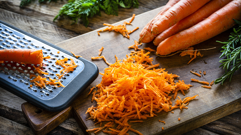 grated carrots and grater on a wood cutting board