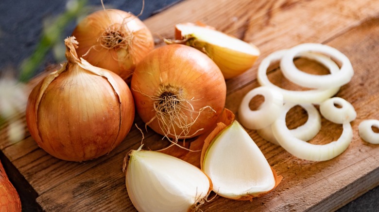 Yellow onions partially sliced on a wooden cutting board.
