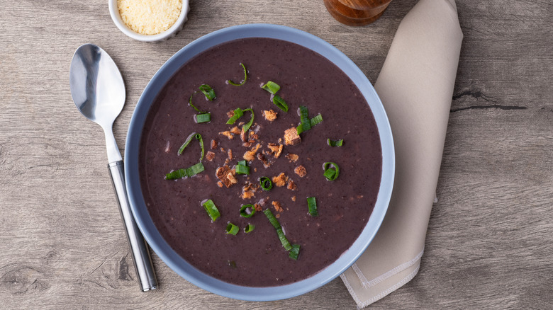 Black bean soup in a bowl with spoon and napkin on wooden table.
