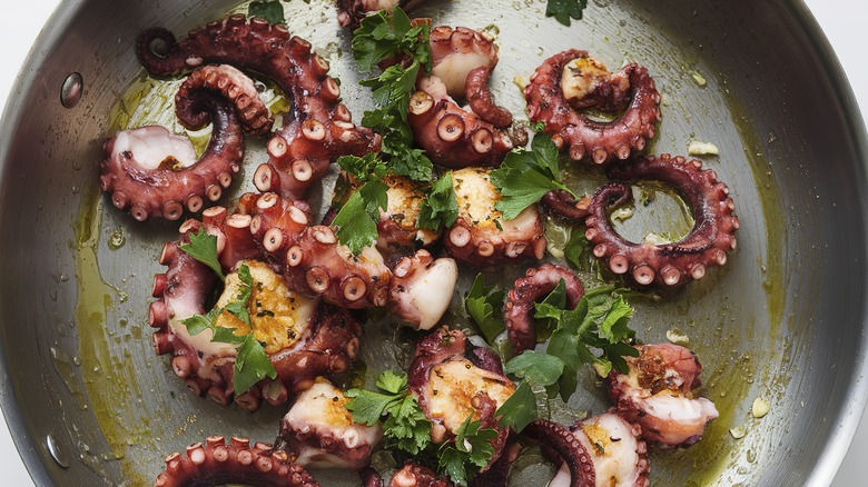 Octopus tentacles cook with herbs in a skillet.