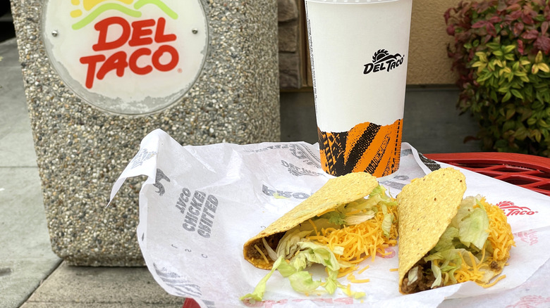 Del Taco tacos and drink next to a Del Taco sign