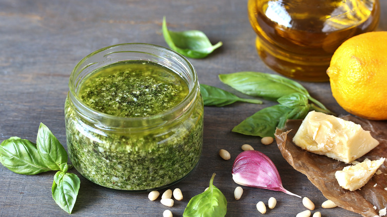 Open jar of pesto with basil, pine nuts, garlic, cheese, lemon, and olive oil