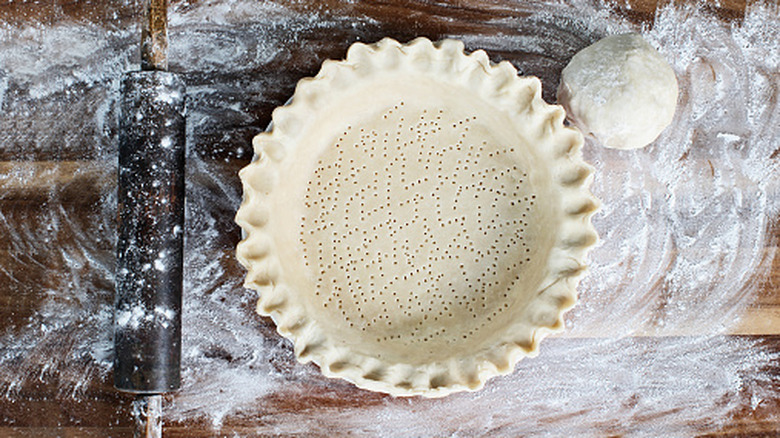 A pie crust surrounded by flour with a rolling pin next to it.