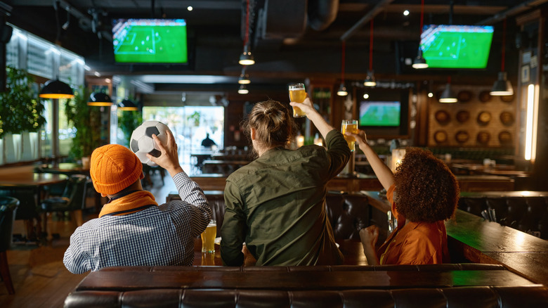 Group of young friends watching football on TV screen at sports bar.