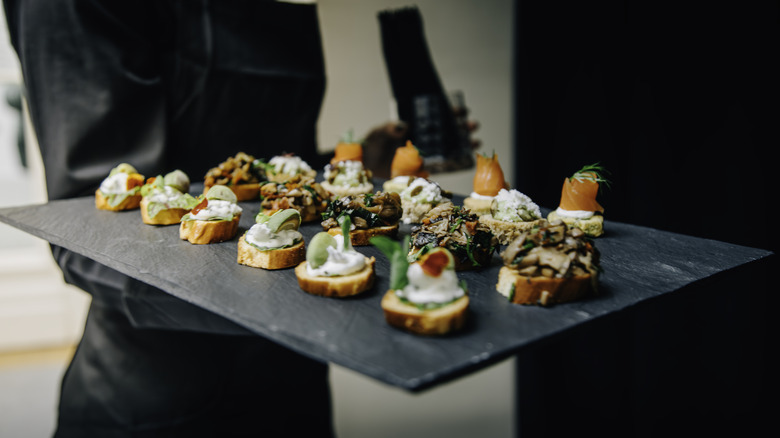 A waiter holding a black slate tray full of a variety of appetizers.