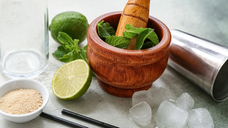 wooden mortar and pestle with mint leaves, lime, and ice
