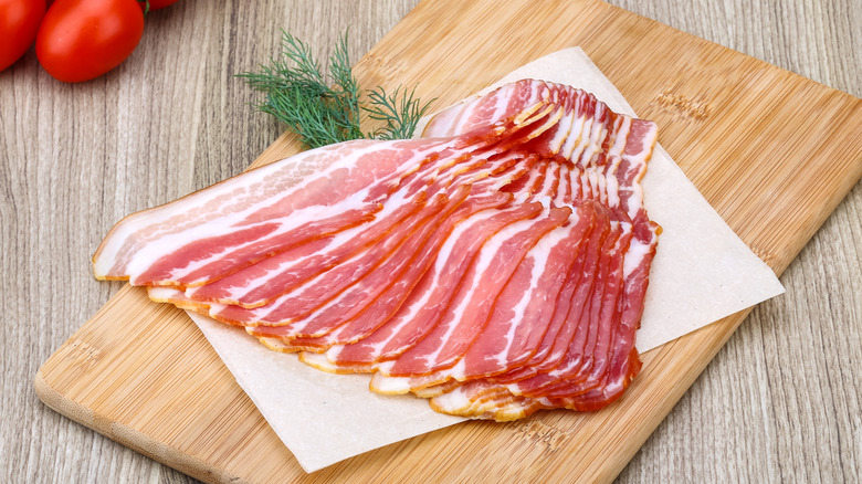 Slices of raw bacon fanned out on a cutting board.