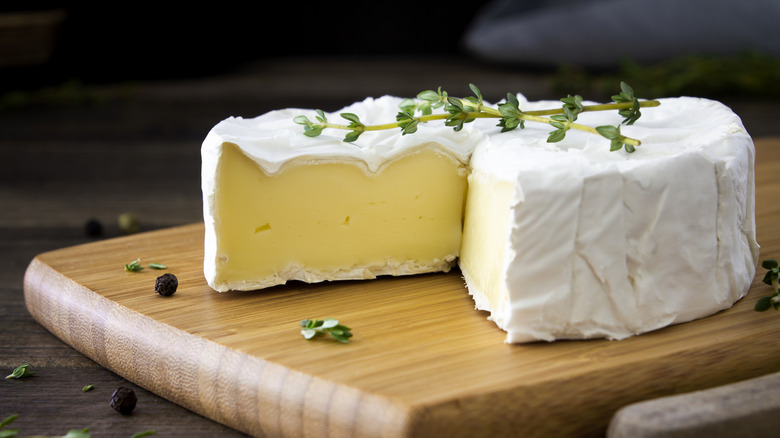 Wheel of brie on a wooden board with fresh herbs