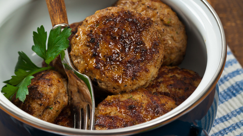 homemade breakfast sausage patties in a blue bowl with a fork and herb garnish