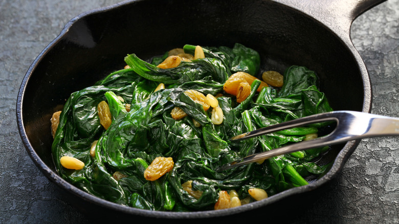 Sauteed spinach with raisins and pine nuts in cast iron pan.
