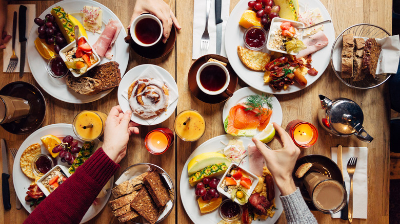 Table filled with breakfast foods, glasses of orange juice, and cups of coffee