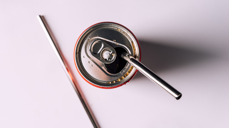 A soda can served with a metal straw is seen from above.