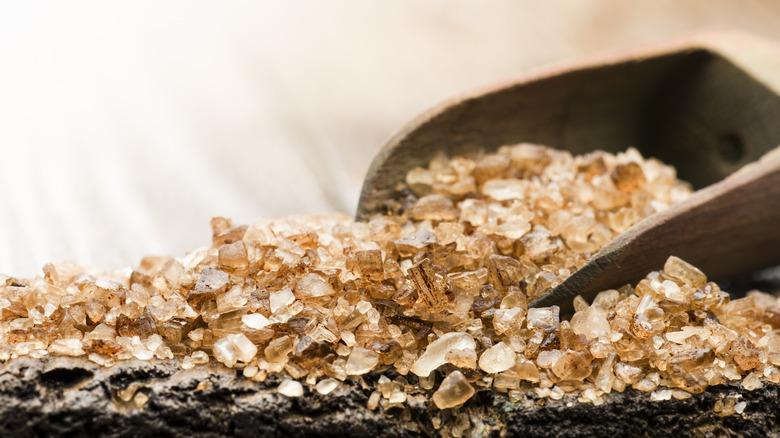 An abundance of smoked salt spills out of a large wooden spoon.