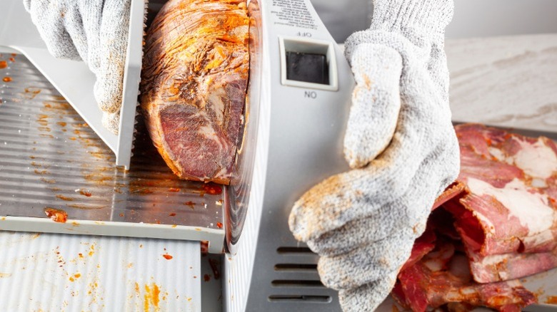 A person uses a meat slicer wearing cutting gloves