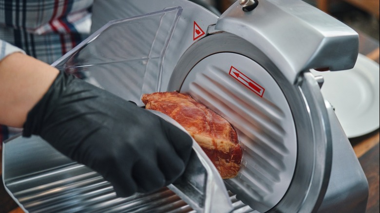 A person using a deli slicer to cut meat