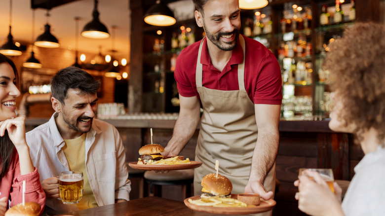 A smiling waiter setting down plates at a restaurant table