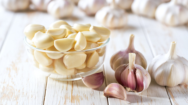 cloves of garlic in a glass bowl next to whole heads of garlic.