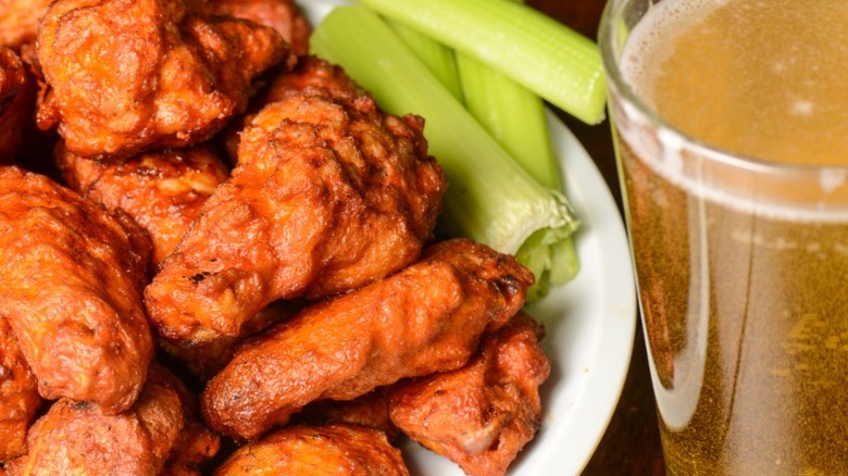 A pint of beer next to a plate of hot wings with celery.