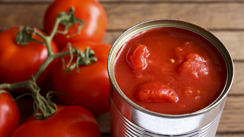 Opened can of tomatoes next to a bunch of fresh tomatoes