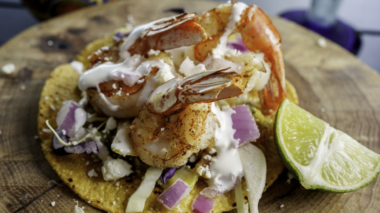 A shrimp taco on a corn tortilla with crema, red onions, cotija and lime.
