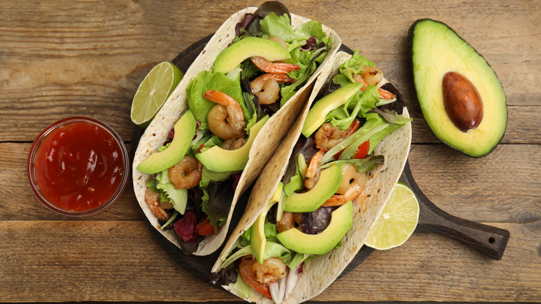 Flat lay of shrimp tacos with avocado and greens in flour tortillas.