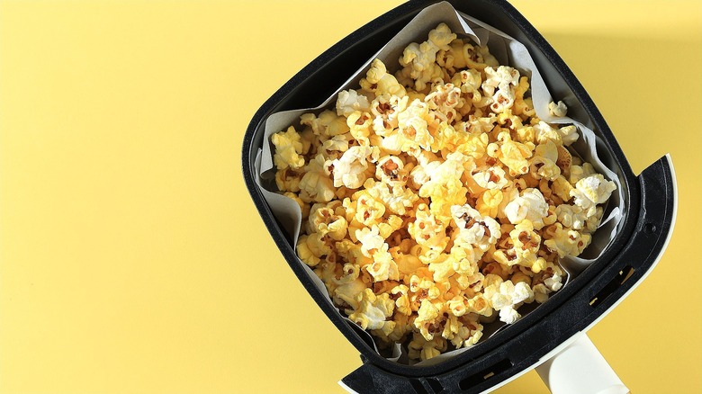 Top-down view of buttered popcorn in an air fryer basket lined with parchment paper over a golden yellow background