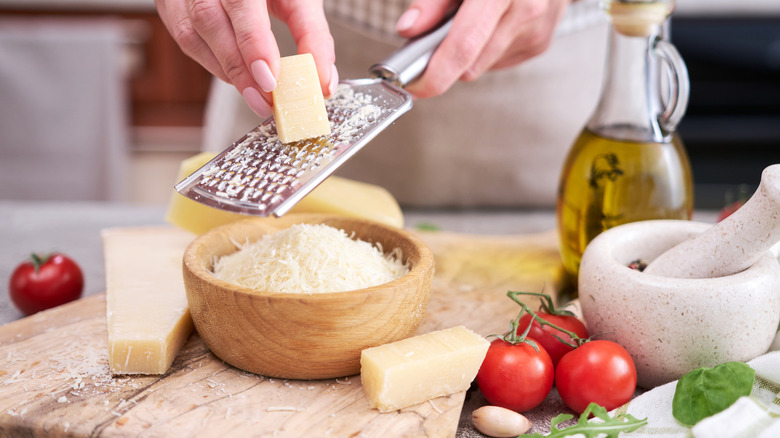 Person grating Parmesan cheese into a wooden bowl