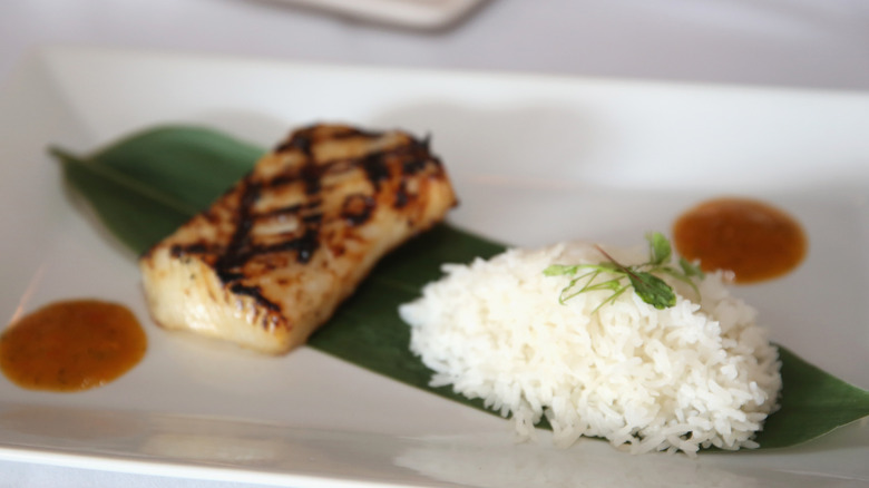A grilled fish dish from Bonefish Grill in Miami Beach with rice on a long green leaf and a white plate with two dollops of sauce